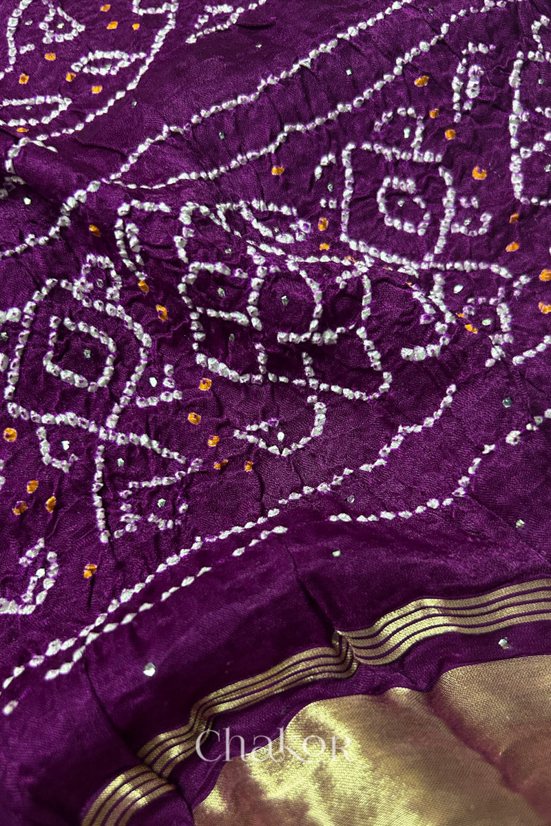 Close-up of a rai bandhej dupatta in magenta featuring white & yellow bandhani dots along with mukaish embroidery.Text reads Chakor brand watermark.
