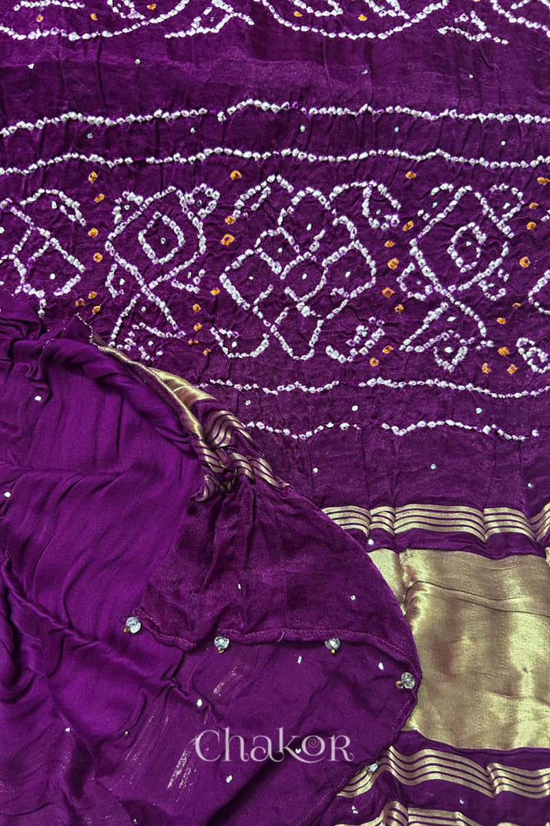 A colourful dupatta showcasing rai bandhej in magenta accented with mukaish work with tissue band folded on corner. Text reads Chakor brand watermark.
