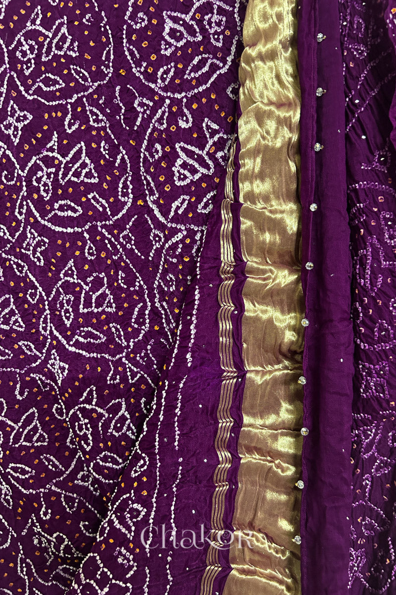 Close-up of a rai bandhej dupatta in magenta featuring white & yellow bandhani dots along with mukaish embroidery & shimmering gold band on pallu.Text reads Chakor brand watermark.
