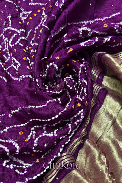 A colourful dupatta showcasing rai bandhej in magenta with golden tissue band placed in swirling style. Text reads Chakor brand watermark.
