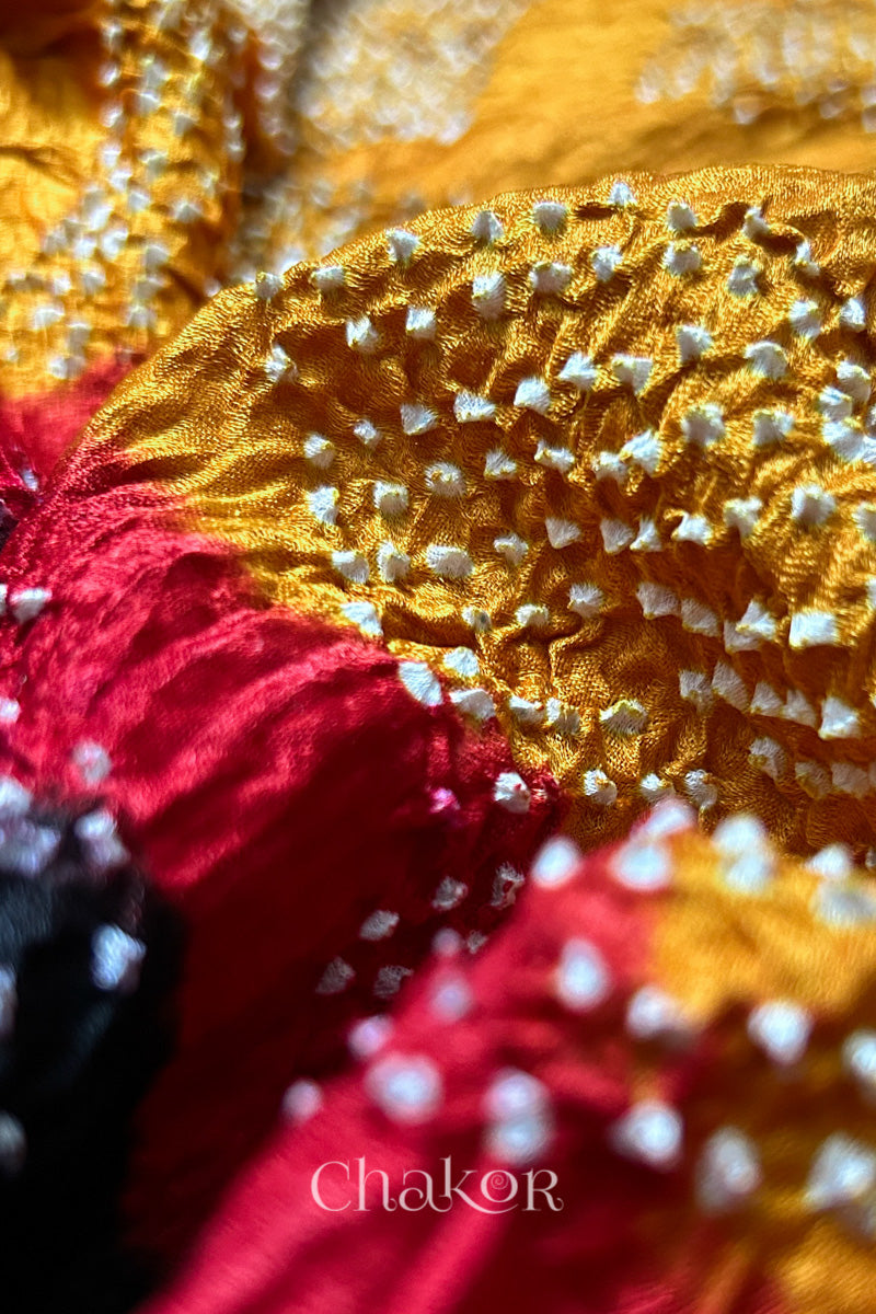 Close-up of a rai bandhej dupatta with red accents along with mustard yellow featuring pearl-like bandhani dots.