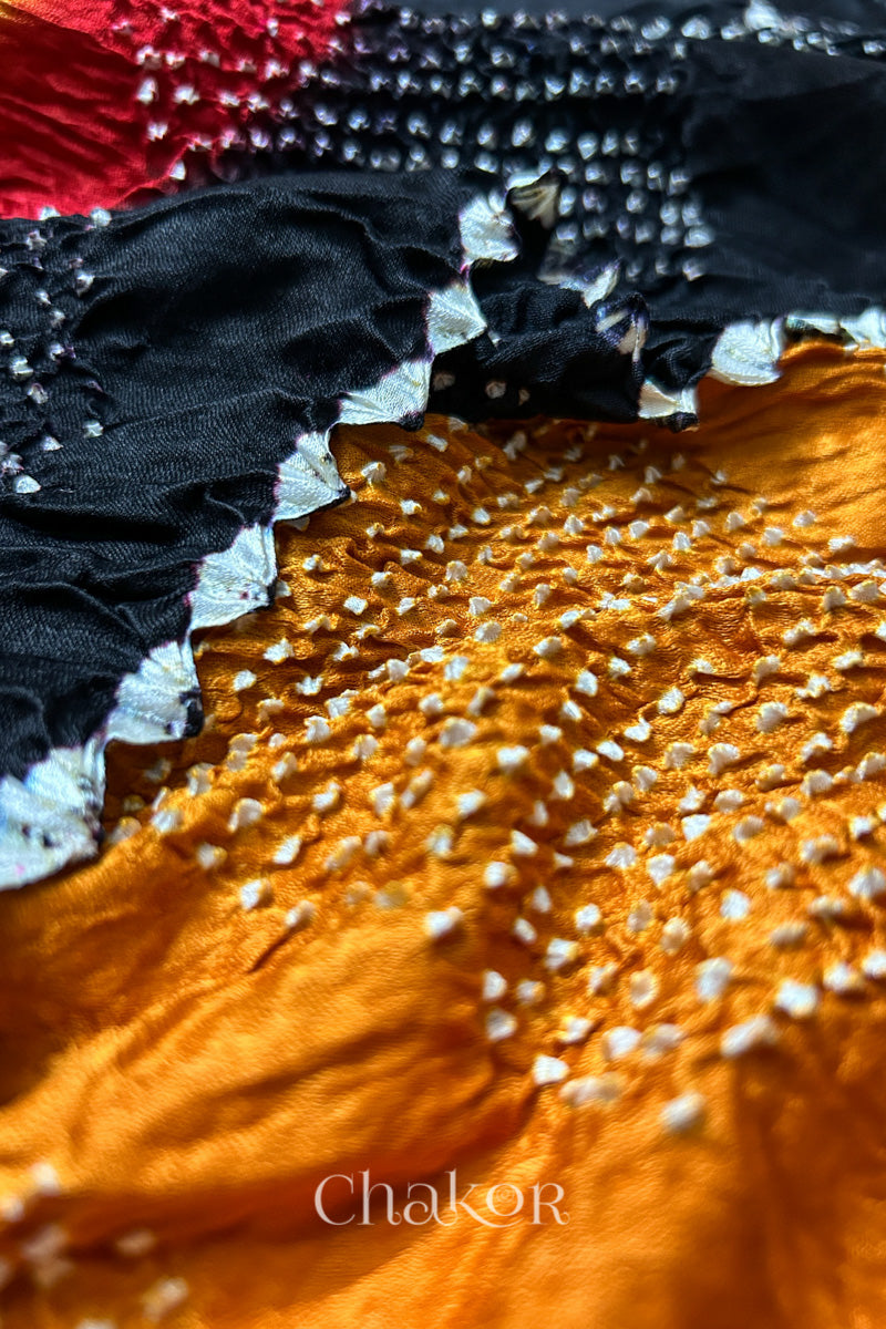Close-up of a rai bandhej dupatta with red accents along with black border & mustard yellow body featuring pearl-like bandhani dots.