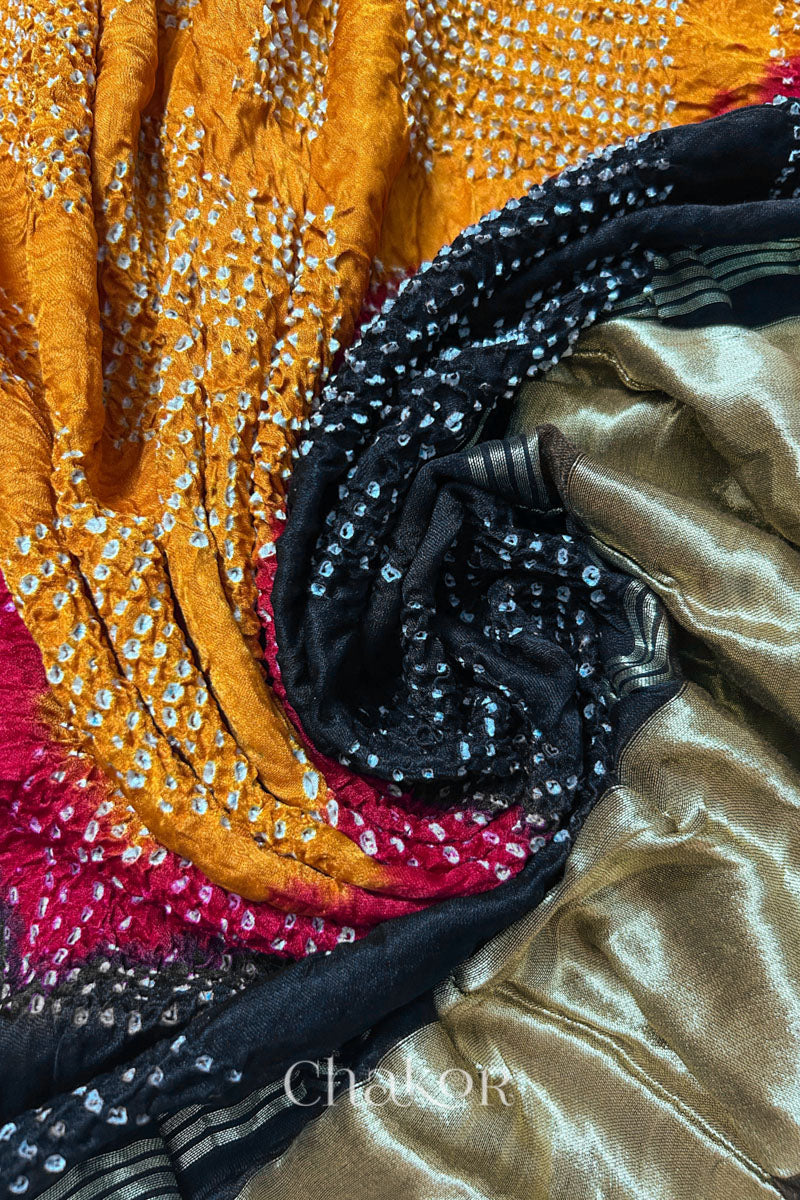 A colourful dupatta showcasing rai bandhej on mustard yellow, red and black pallu with tissue placed in swirling style. Text reads Chakor brand watermark.