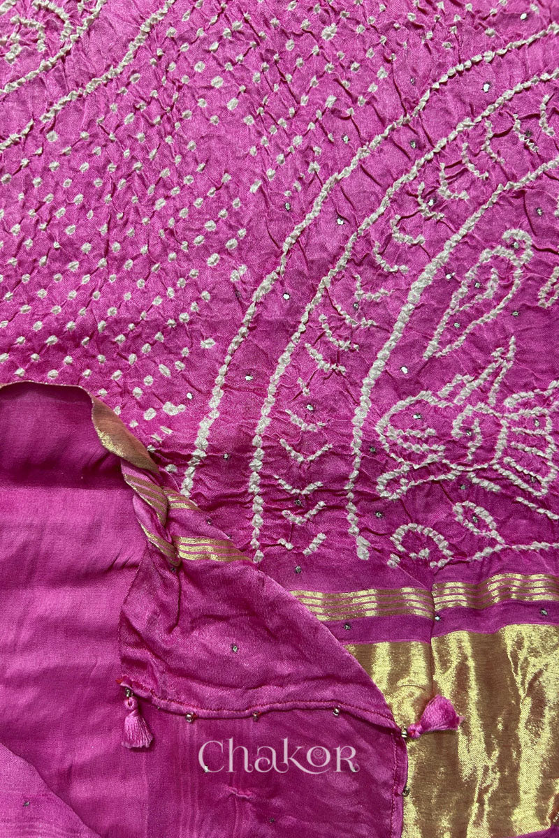 A colourful dupatta showcasing rai bandhej in pink ombre dyed accented with mukaish work with tissue band folded on corner. Text reads Chakor brand watermark.
