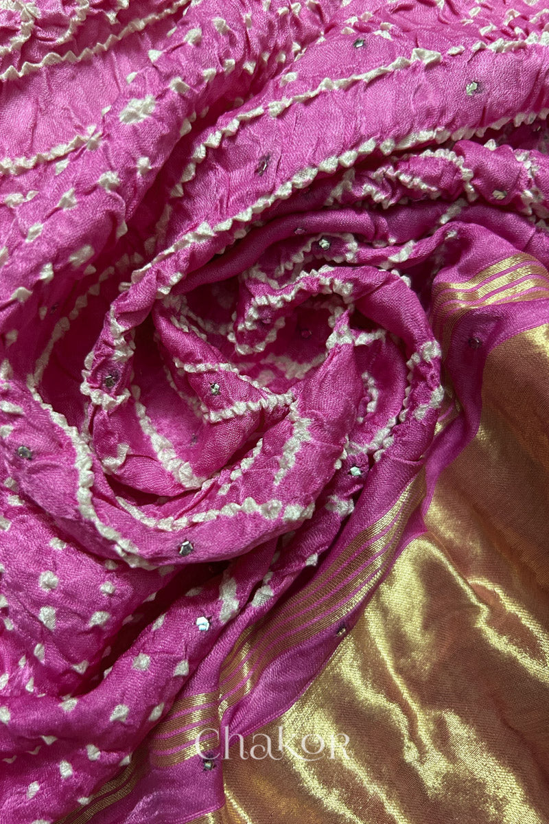 A colourful dupatta showcasing rai bandhej in pink ombre dyed with golden tissue band placed in swirling style. Text reads Chakor brand watermark.
