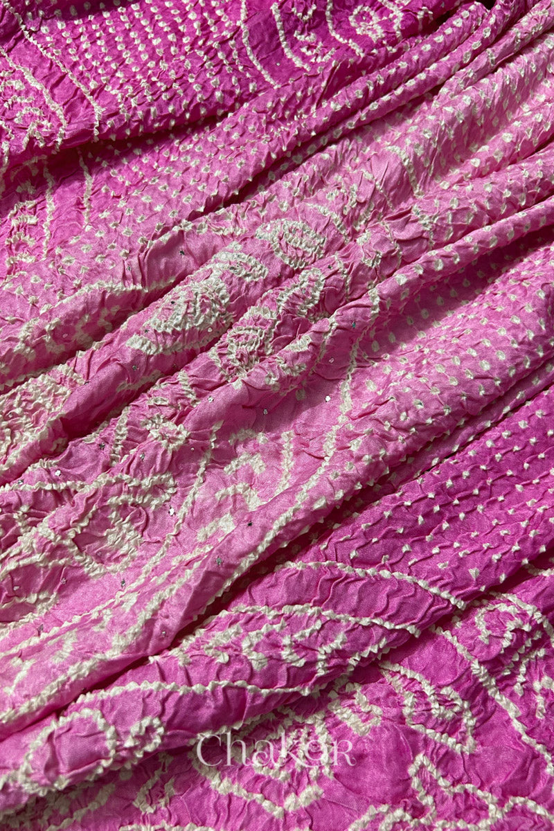 Close-up of a rai bandhej dupatta in pink ombre dyed featuring white bandhani dots along with mukaish embroidery.Text reads Chakor brand watermark.
