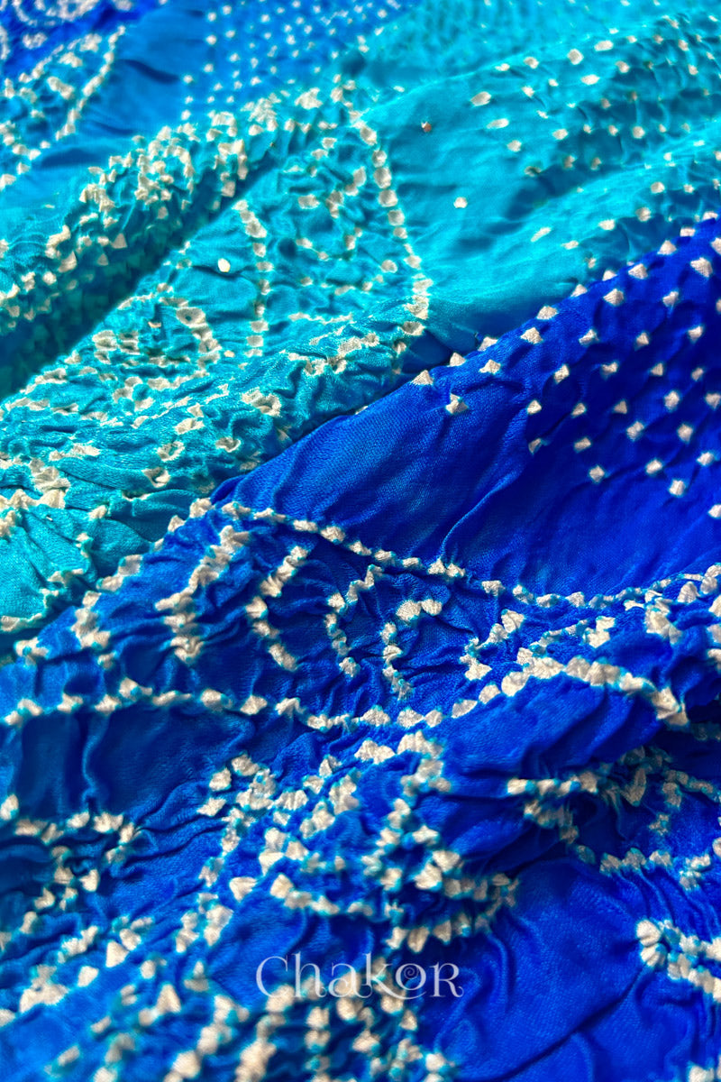 Close-up of a rai bandhej dupatta in blue ombre dyed featuring white bandhani dots along with mukaish embroidery.Text reads Chakor brand watermark.

