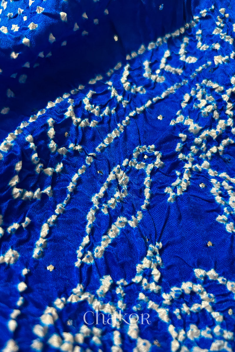 Close-up of a rai bandhej dupatta in blue ombre dyed featuring white bandhani dots along with mukaish embroidery.Text reads Chakor brand watermark.
