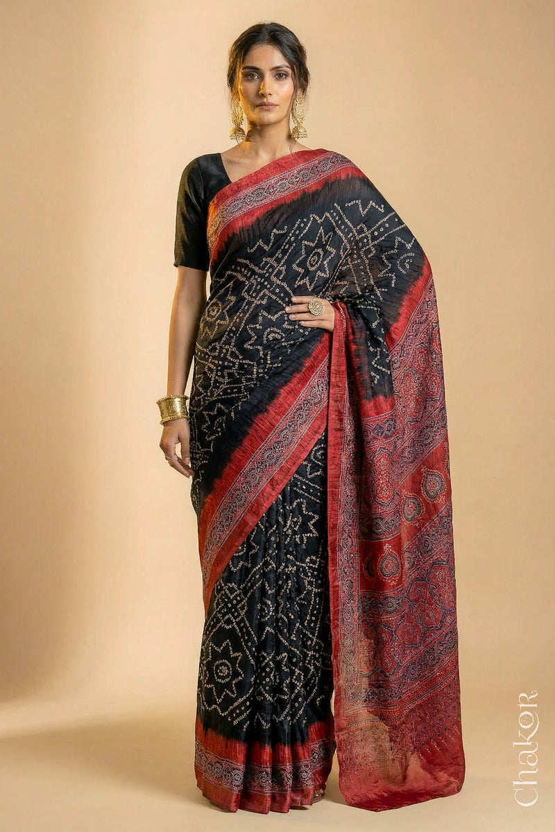 Woman wearing Black Bandhani Saree with Natural Red Ajrakh printed border and pallu in pure gaji silk with traditional bandhej tie-dye, handcrafted in Kutch. 