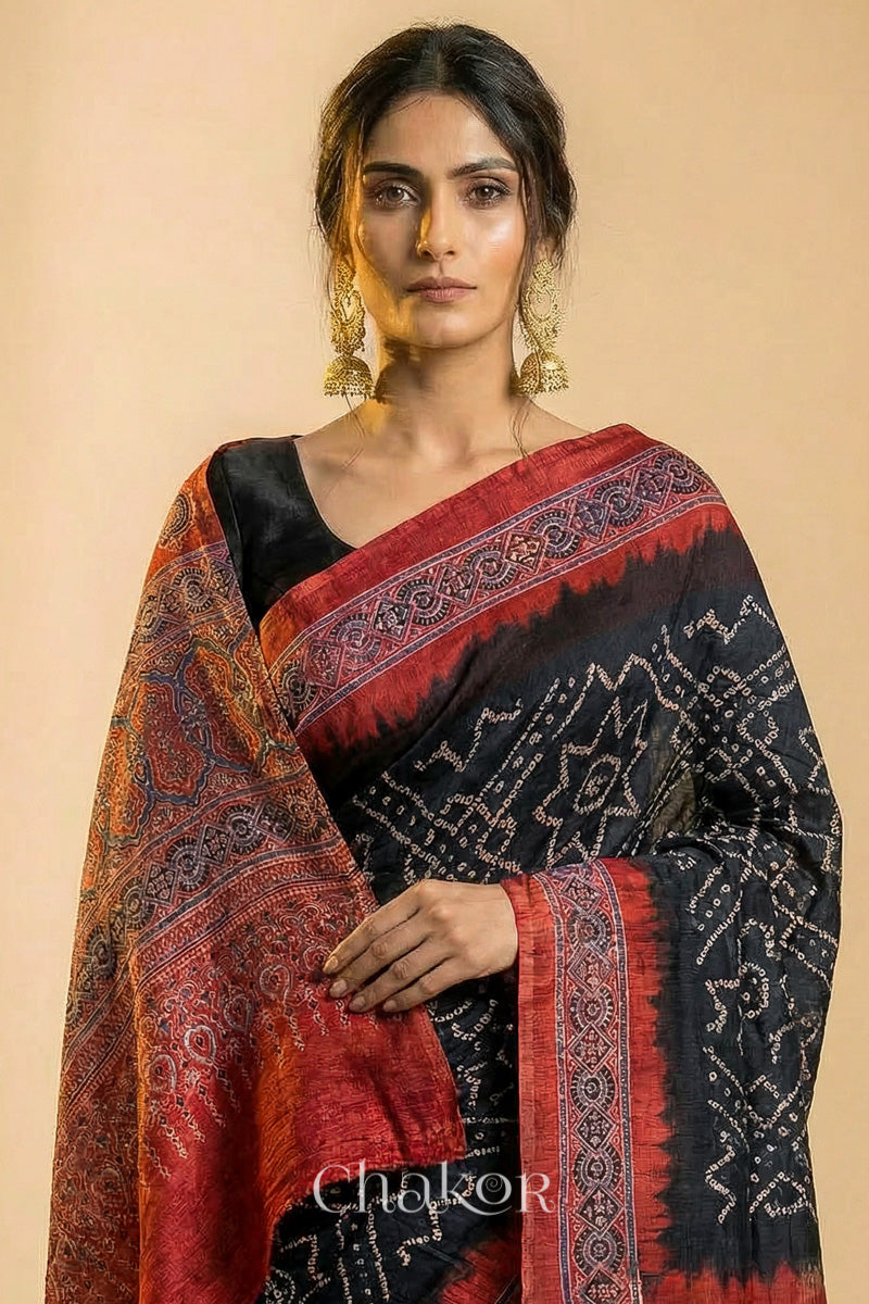 Woman wearing Black Bandhani Saree with Natural Red Ajrakh printed border and pallu in pure gaji silk with traditional bandhej tie-dye, handcrafted in Kutch. 