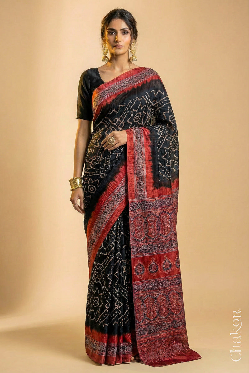 Woman wearing Black Bandhani Saree with Natural Red Ajrakh printed border and pallu in pure gaji silk with traditional bandhej tie-dye, handcrafted in Kutch. 