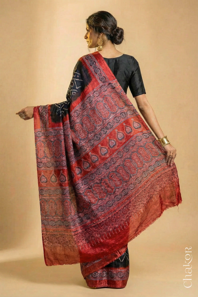 Woman wearing Black Bandhani Saree with Natural Red Ajrakh printed border and pallu in pure gaji silk with traditional bandhej tie-dye, handcrafted in Kutch. 