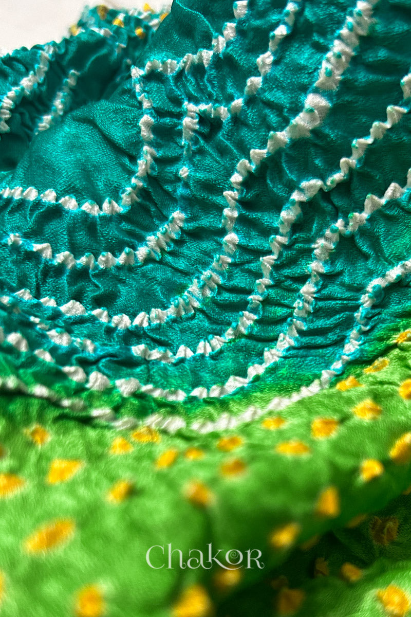 Close-up of a rai bandhej dupatta in Jade & parrot green dual colour featuring white & yellow bandhani dots.Text reads Chakor brand watermark.
