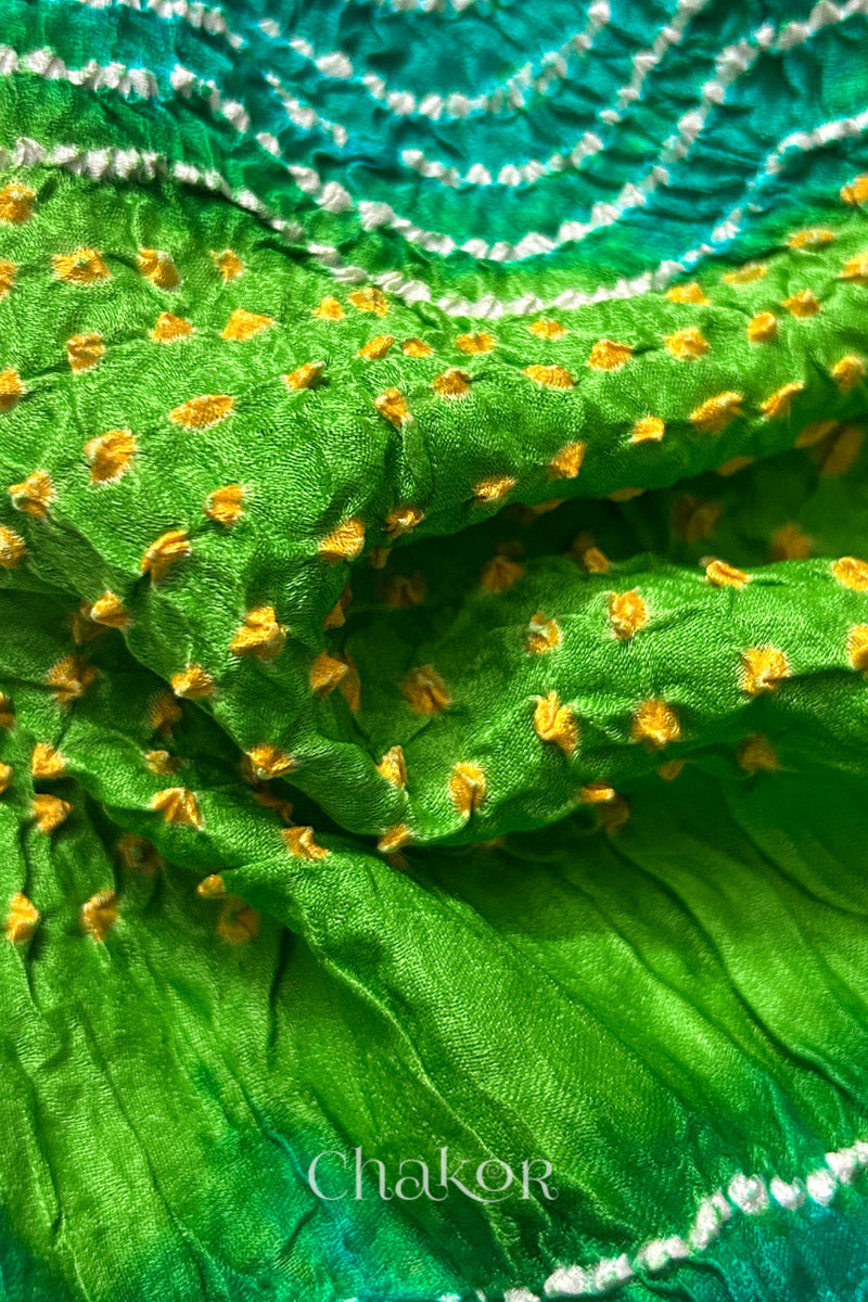 Close-up of a rai bandhej dupatta in Jade & parrot green dual colour featuring white & yellow bandhani dots.Text reads Chakor brand watermark.
