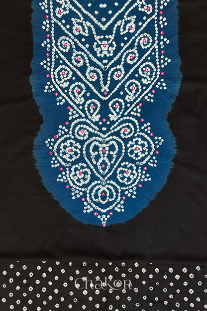 Close-up of tie dyed black kurta fabric featuring intricate bandhani and embroidered on contrasting indigo blue yoke with matching bandhani dotted bottom fabric, with Chakor brand logo.

