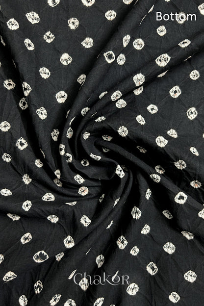 Close-up of black fabric featuring bandhani pattern of white dots, arranged in a swirly style showcasing the textile's texture and design details.Text reads bottom details.
