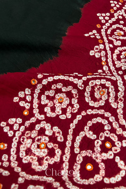 Close-up of  black fabric adorned with intricate traditional bandhani patterns and mirror embroidery on red yoke, showcasing beautiful craftsmanship.