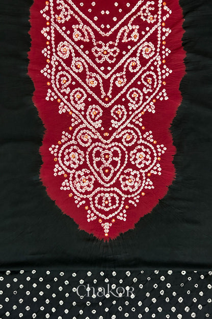 Close-up of tie dyed black kurta fabric featuring intricate bandhani and embroidered on contrasting red yoke with matching bandhani dotted bottom fabric, with Chakor brand logo.
