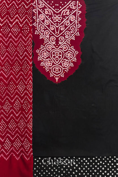 A  black kurta set fabric with intricate bandhani & mirror embroidered contrast yoke, paired with a matching bottom & contrast red odhani placed on the left side featuring a zigzag design.

