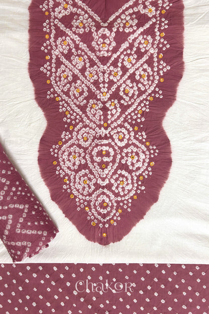 A stylish set fabric featuring a soft rose pink mirror embroidered yoke on a white kurta, bandhani soft rose pink bottom and dupatta rolled beautifully and placed on the fabric. Text reads Chakor.
