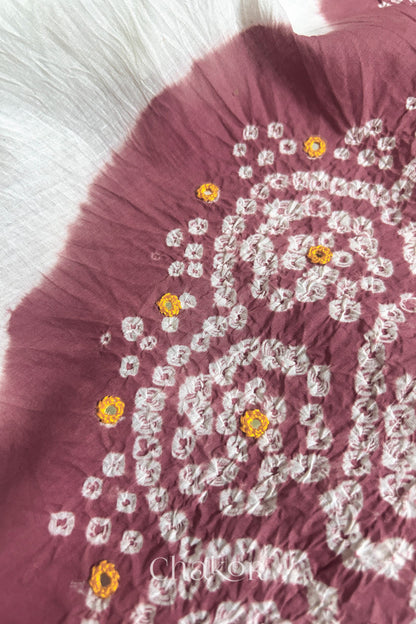 Close-up of soft rose pink-white fabric adorned with intricate traditional bandhani patterns and yellow mirror embroidery, showcasing beautiful craftsmanship.