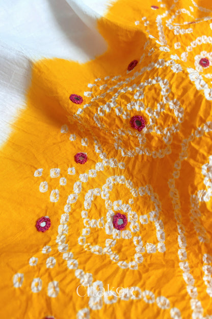 Close-up of yellow-white fabric adorned with intricate traditional bandhani patterns and pink mirror embroidery, showcasing beautiful craftsmanship.