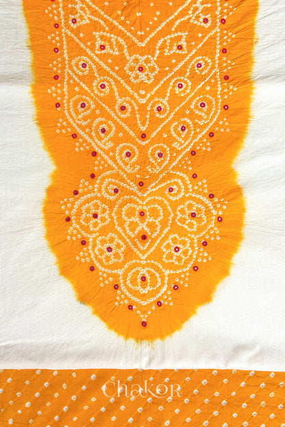 Close-up of tie dyed yellow yoke on white kurta fabric featuring intricate bandhani and embroidered patterns with yellow bandhani dotted bottom fabric, with Chakor brand logo.