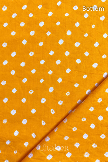 Close up of Bottom fabric in yellow patterned with bandhani tie dye dots, folded at the corner displaying texture and detail.