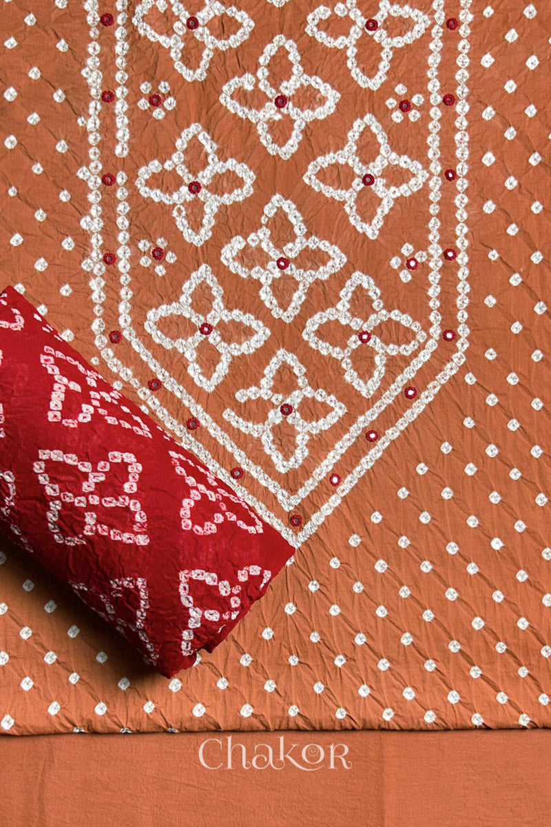 Front yoke detail of Brick Orange Bandhani cotton kurta fabric with hand embroidery and mirror work and Red dupatta rolled up.
