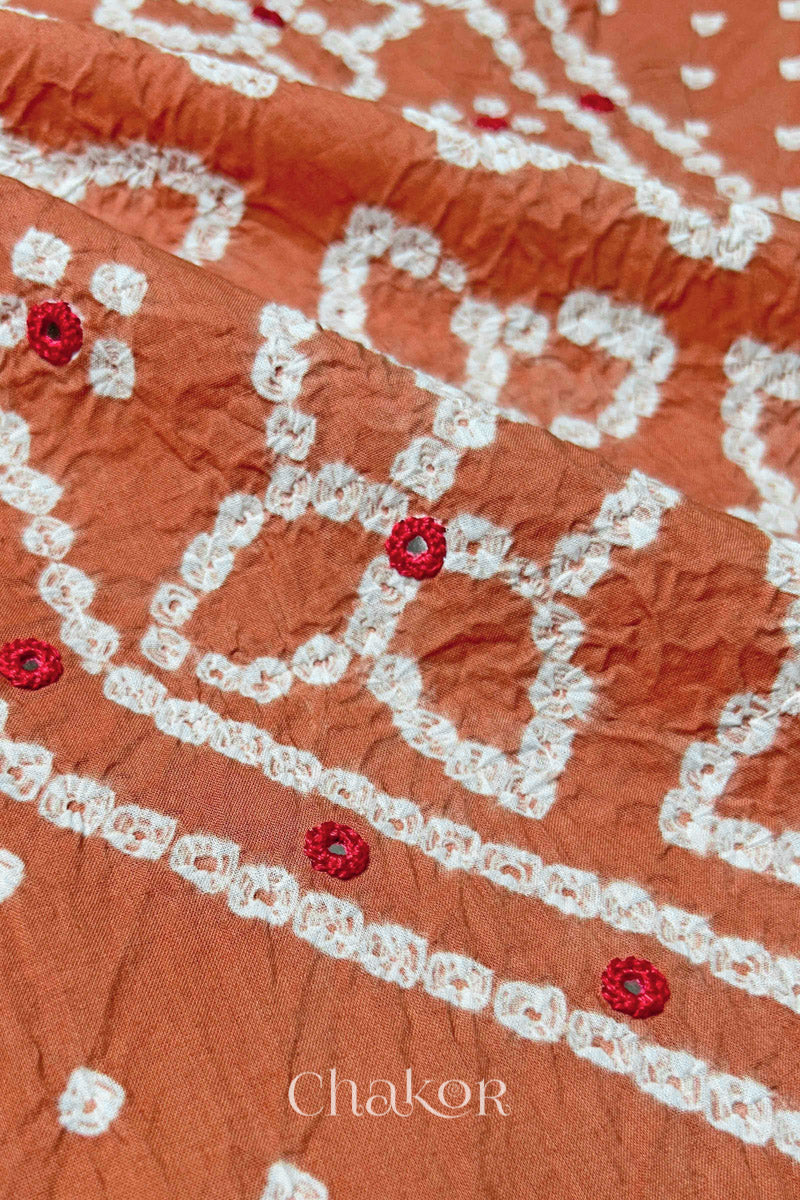 Hand tied Bandhani floral motif with colourful mirror embroidery on Brick Orange cotton fabric.
