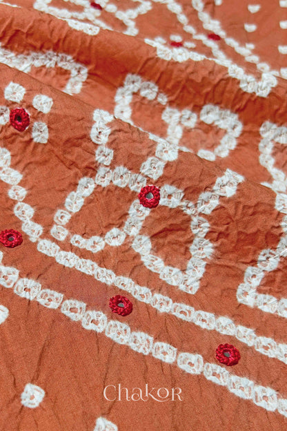 Hand tied Bandhani floral motif with colourful mirror embroidery on Brick Orange cotton fabric.
