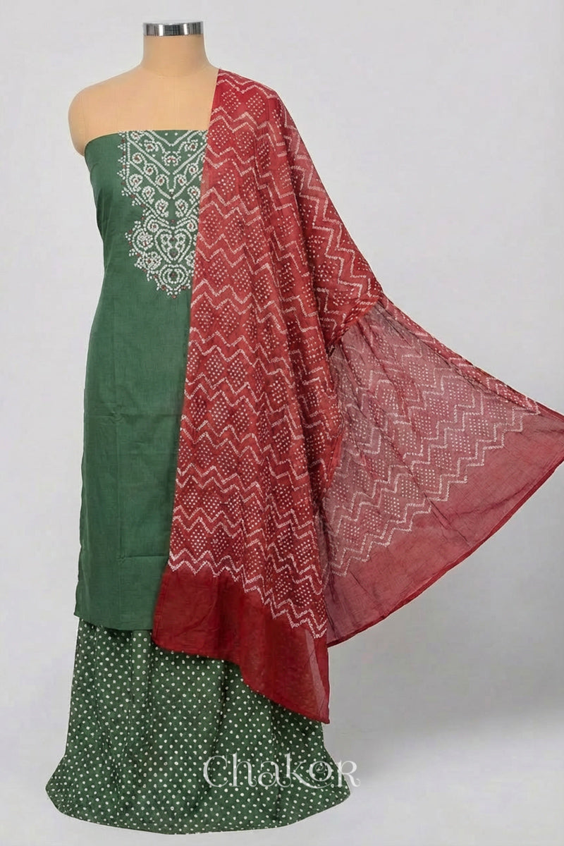 A stylish moss green set fabric featuring mirror embroidered yoke, bandhani bottom and contrast brick red dupatta draped on a mannequin.