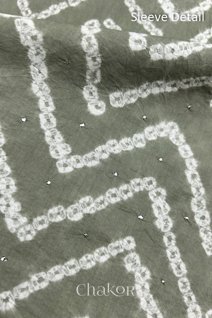 Close-up of  black bandhani fabric featuring chevron tie-dye design, showcasing sparkly mukaish embroidery with Chakor brand watermark. Text reads sleeve details.
