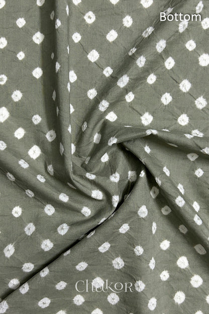 Close-up of cement grey fabric featuring bandhani pattern of white dots, arranged in a swirly style showcasing the textile's texture and design details.Text reads bottom details.
