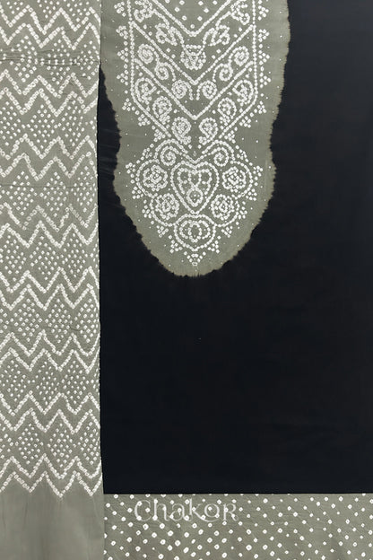 A  black kurta set fabric with intricate bandhani & cement grey yoke with sparkly mukaish embroidery, paired with a bottom & odhani placed on the left side featuring a zigzag design.
