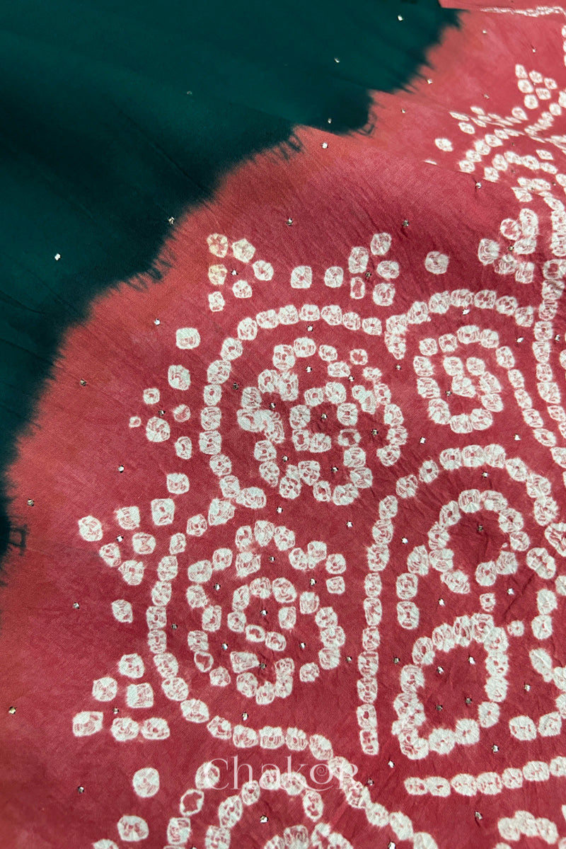 Close-up of dark green fabric adorned with intricate traditional bandhani patterns and sparkly mukaish embroidery on dusty red yoke, showcasing beautiful craftsmanship.