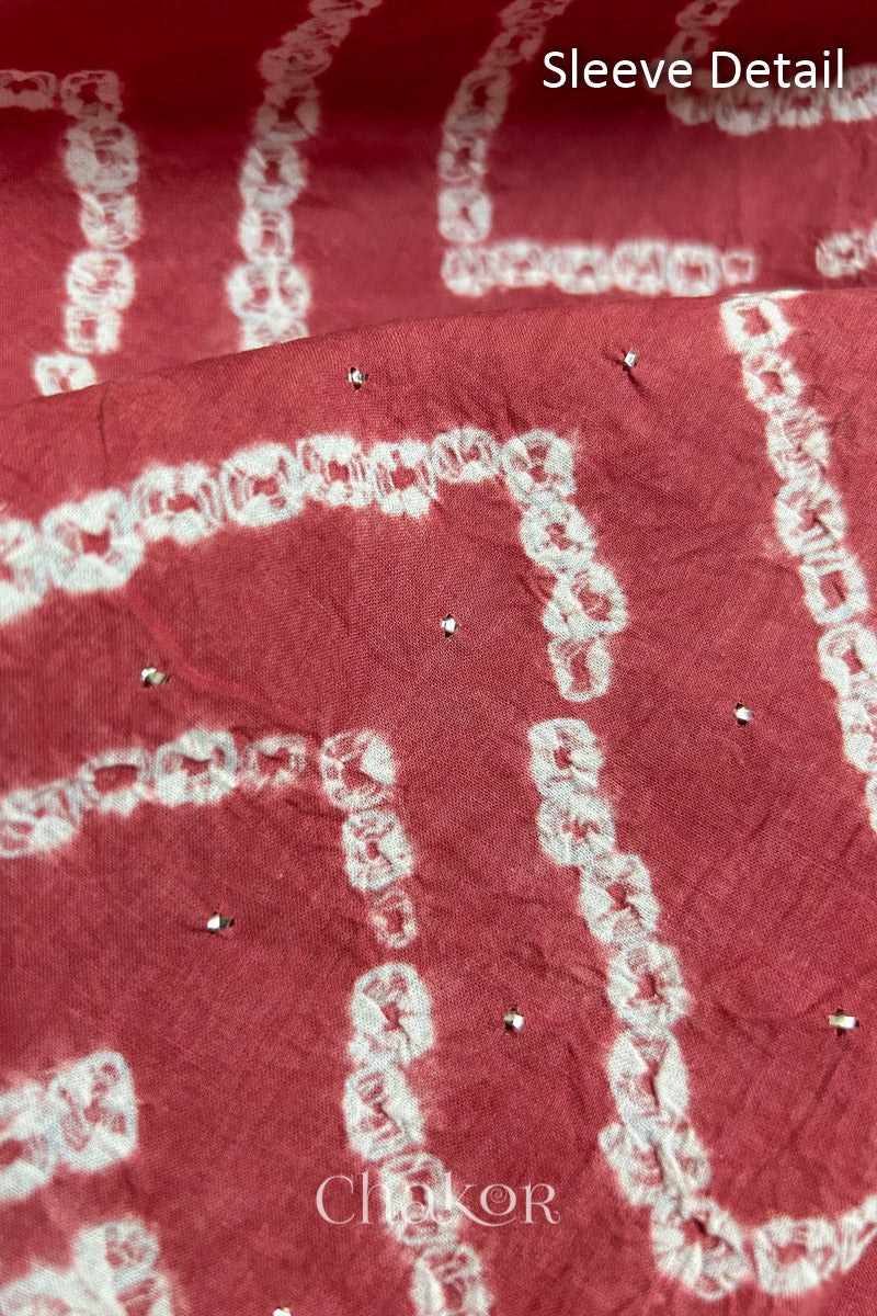 Close-up of dusty red bandhani fabric featuring chevron tie-dye design, showcasing sparkly mukaish embroidery with Chakor brand watermark. Text reads sleeve details.