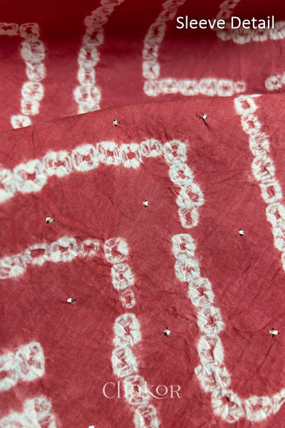 Close-up of dusty red bandhani fabric featuring chevron tie-dye design, showcasing sparkly mukaish embroidery with Chakor brand watermark. Text reads sleeve details.