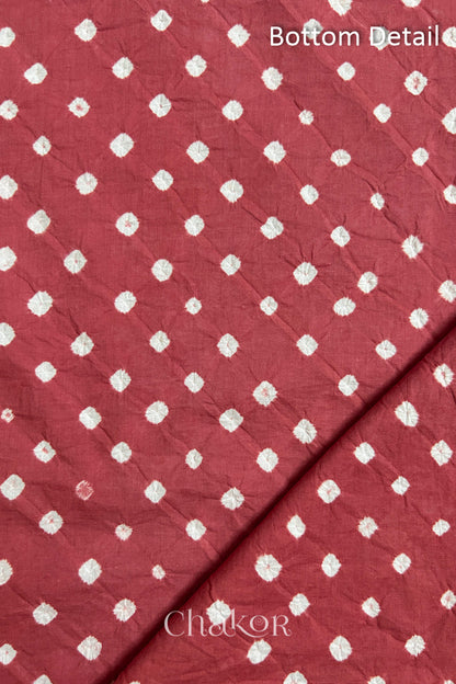 Close up of bottom fabric in dusty red patterned with bandhani tie dye dots, folded at the corner displaying texture and detail. Text reads bottom.
