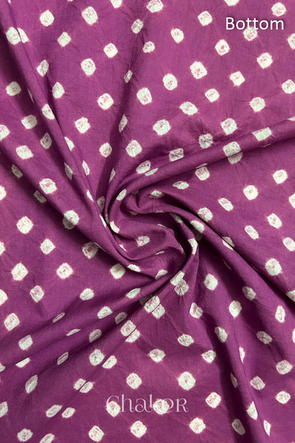 Close-up of violet puprle fabric featuring bandhani pattern of white dots, arranged in a swirly style showcasing the textile's texture and design details.Text reads bottom details.

