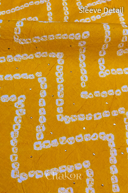 Close-up of yellow bandhani fabric featuring chevron tie-dye design, showcasing sparkly mukaish embroidery with Chakor brand watermark. Text reads sleeve details.
