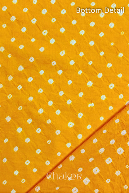 Close up of bottom fabric in yellow patterned with bandhani tie dye dots, folded at the corner displaying texture and detail. Text reads bottom.
