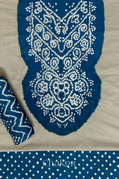 A classic light grey set fabric featuring sparkly mukaish embroidered contrast indigo blue yoke & bottom and dupatta rolled beautifully and placed on the fabric. Text reads Chakor.
