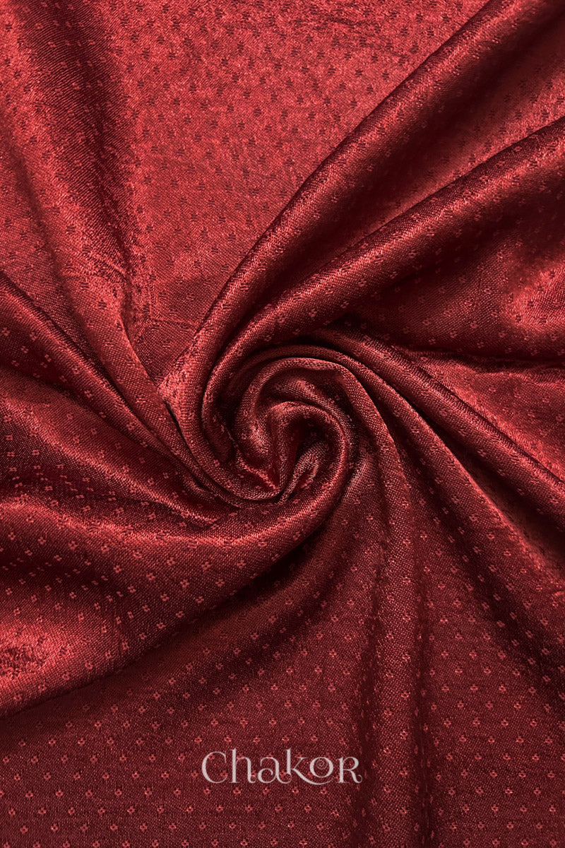 Close-up of brick red mashru self textured fabric arranged in a swirling design with 'Chakor' logo visible.