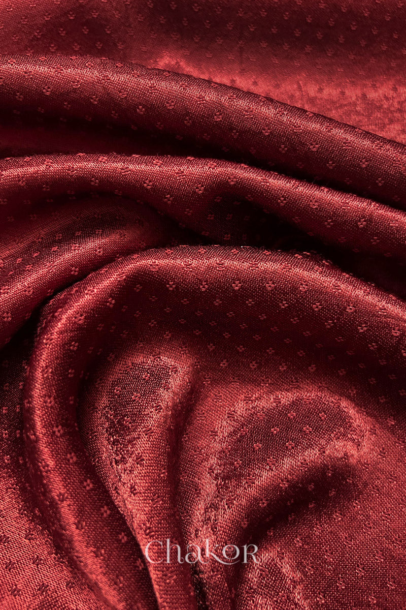 Close-up of brick red mashru self textured fabric with 'Chakor' logo visible.
