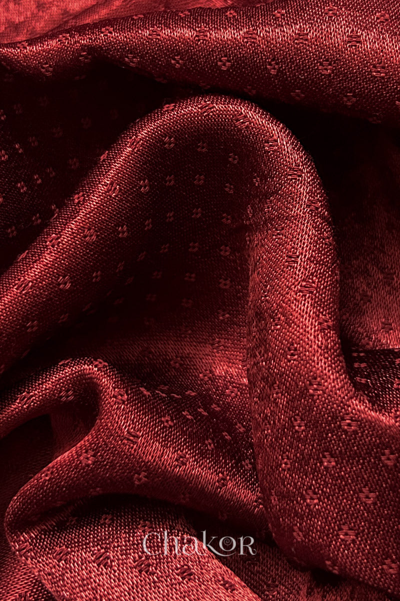 Close-up of brick red mashru self textured fabric with 'Chakor' logo visible.
