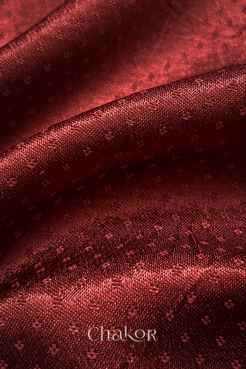 Close-up of brick red mashru self textured fabric with 'Chakor' logo visible.
