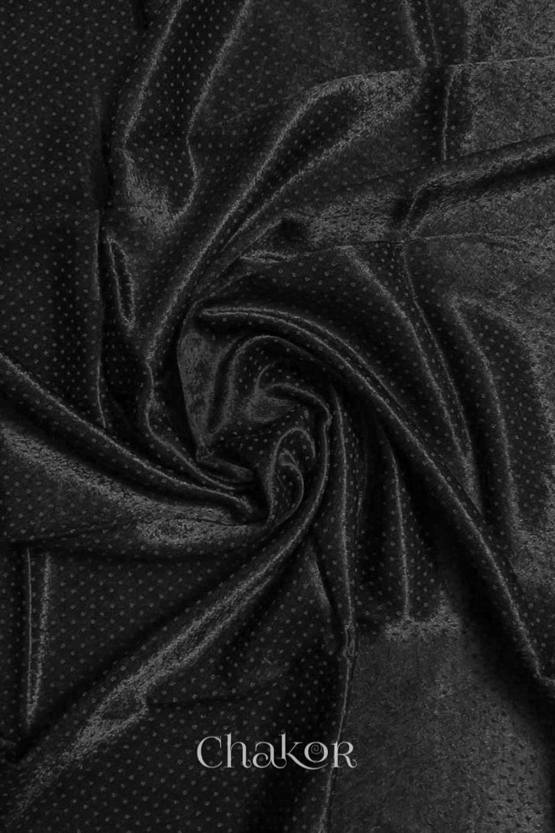 Close-up of black mashru self textured fabric arranged in a swirling design with 'Chakor' logo visible.