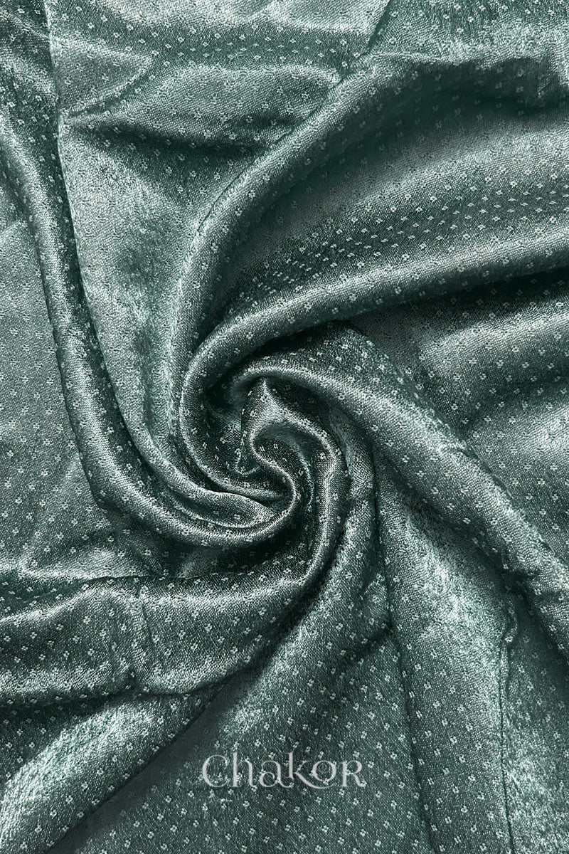 Close-up of Charcoal grey mashru self textured fabric arranged in a swirling design with 'Chakor' logo visible.