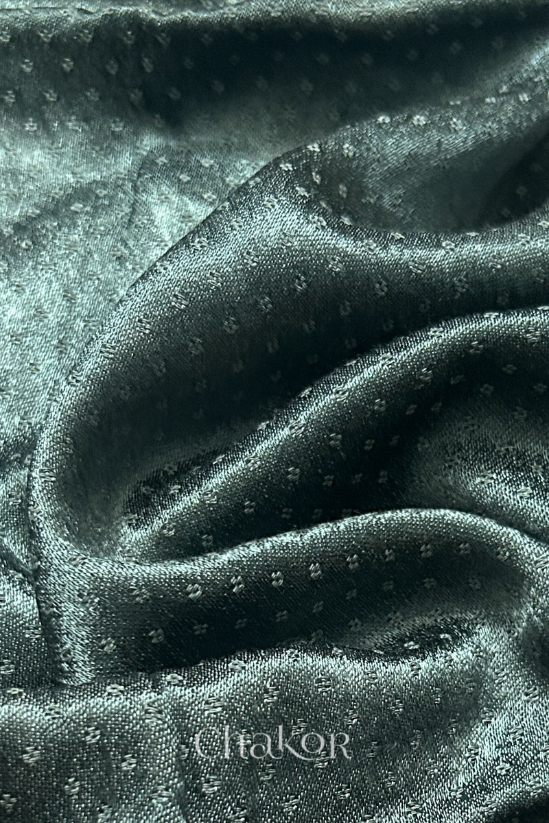 Close-up of charcoal grey mashru self textured fabric with 'Chakor' logo visible.
